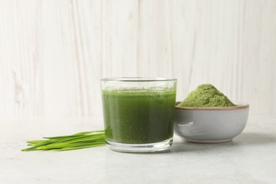 Wheat grass drink in glass, fresh sprouts and bowl of green powder on light table