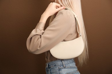 Woman with stylish baguette handbag on brown background, closeup