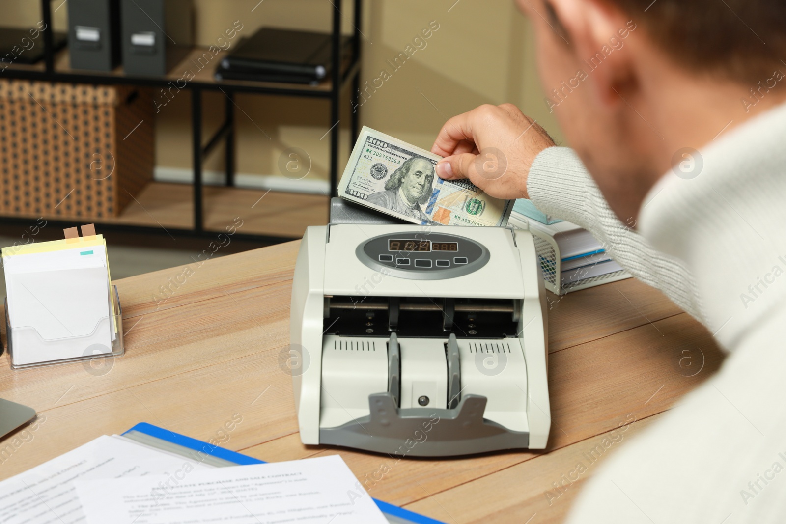 Photo of Man putting money into banknote counter at wooden table indoors, closeup