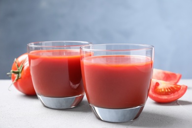 Photo of Delicious fresh tomato juice on light grey table against light blue background, closeup