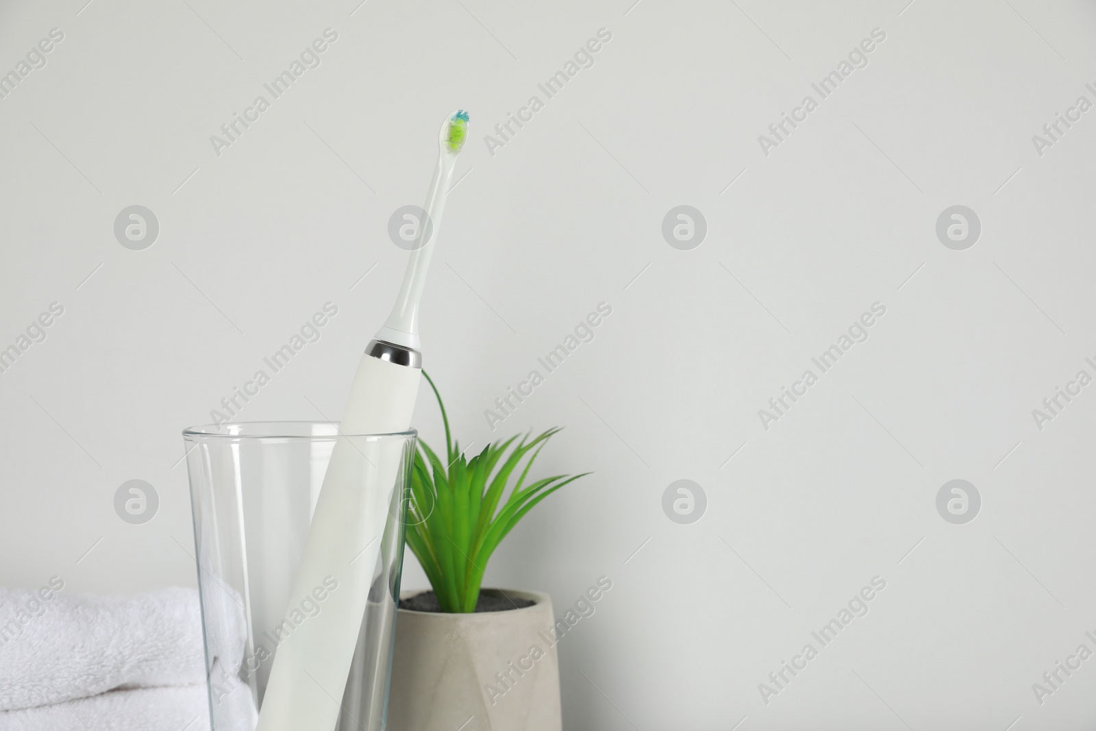 Photo of Electric toothbrush in glass and green houseplant on light background. Space for text