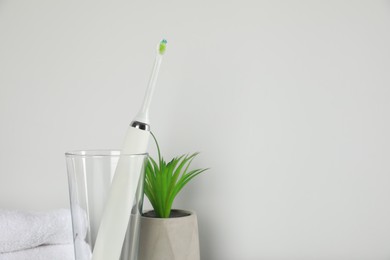 Electric toothbrush in glass and green houseplant on light background. Space for text