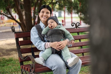 Mother holding her child in sling (baby carrier) on bench in park