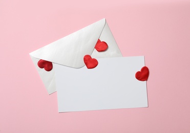 Photo of Blank card, envelope and red decorative hearts on pink background, flat lay with space for text. Valentine's Day celebration