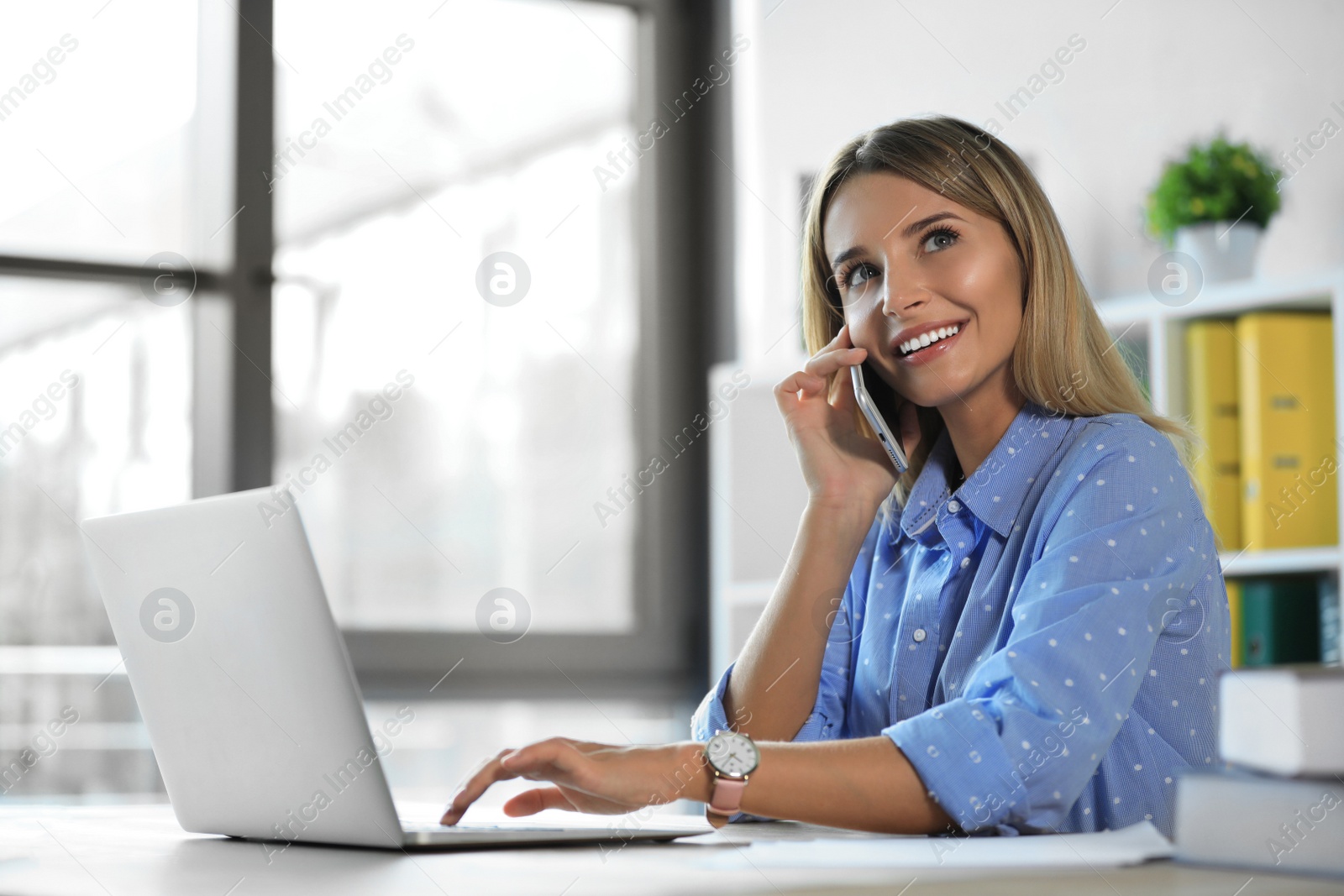 Photo of Female business trainer talking on phone while working with laptop in office