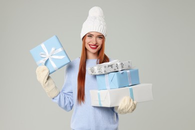 Photo of Young woman in hat and sweater with Christmas gifts on light grey background