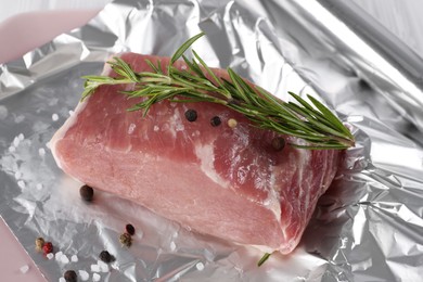 Photo of Aluminum foil with raw meat, rosemary and spices on white table, closeup