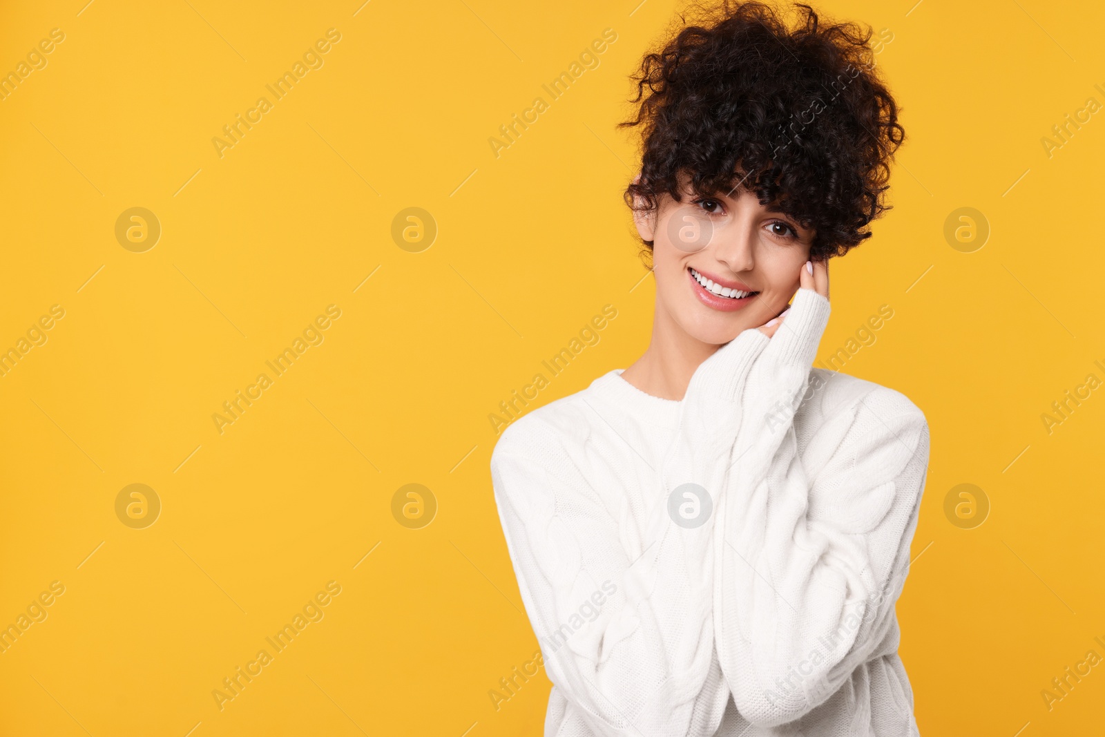 Photo of Happy young woman in stylish white sweater on yellow background, space for text