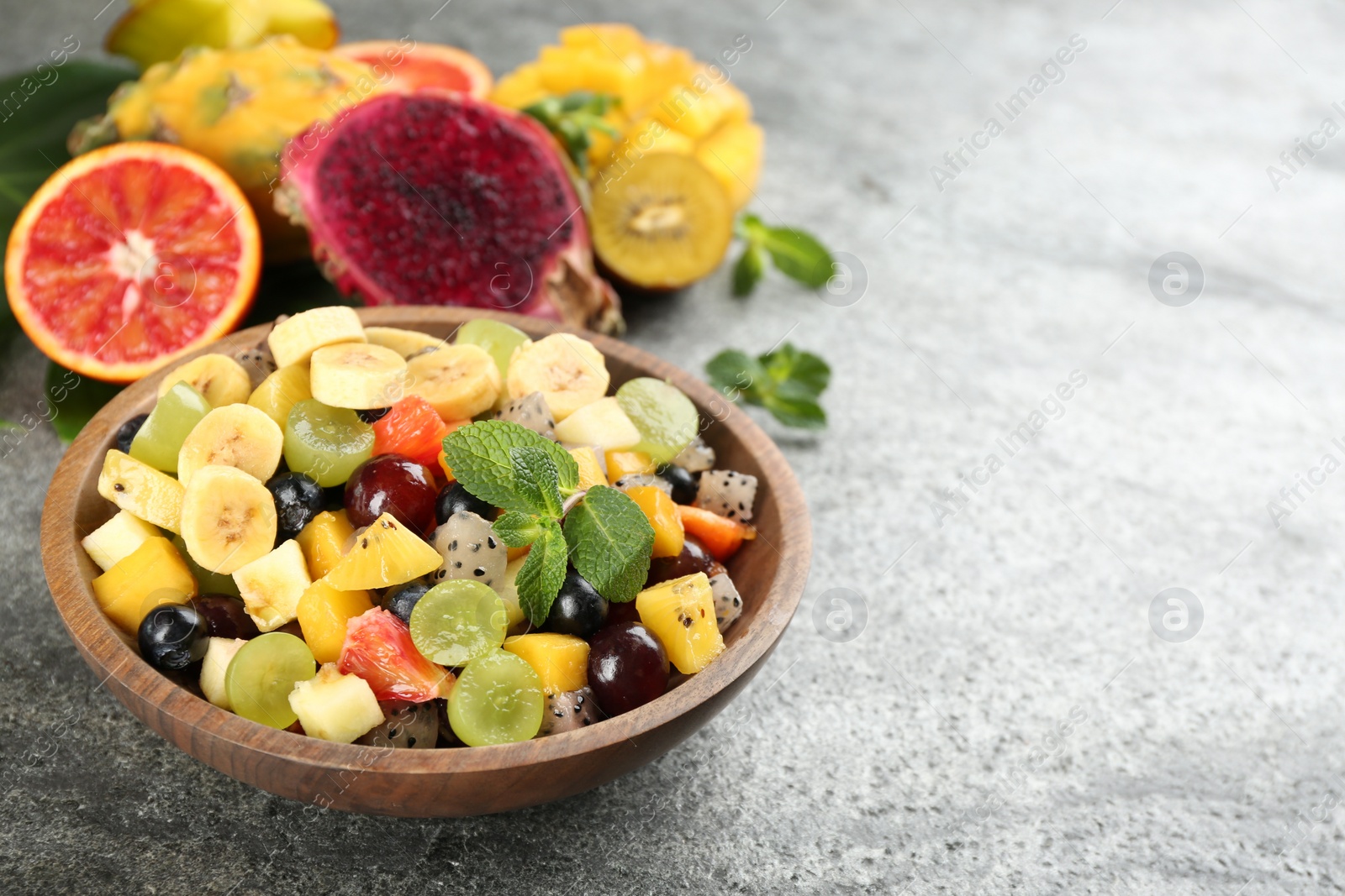 Photo of Delicious exotic fruit salad and ingredients on grey table. Space for text