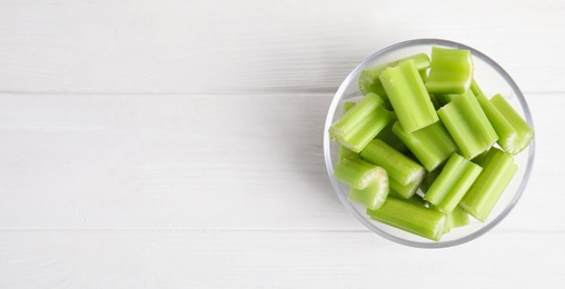 Cut celery in glass bowl on white wooden table, top view. Space for text