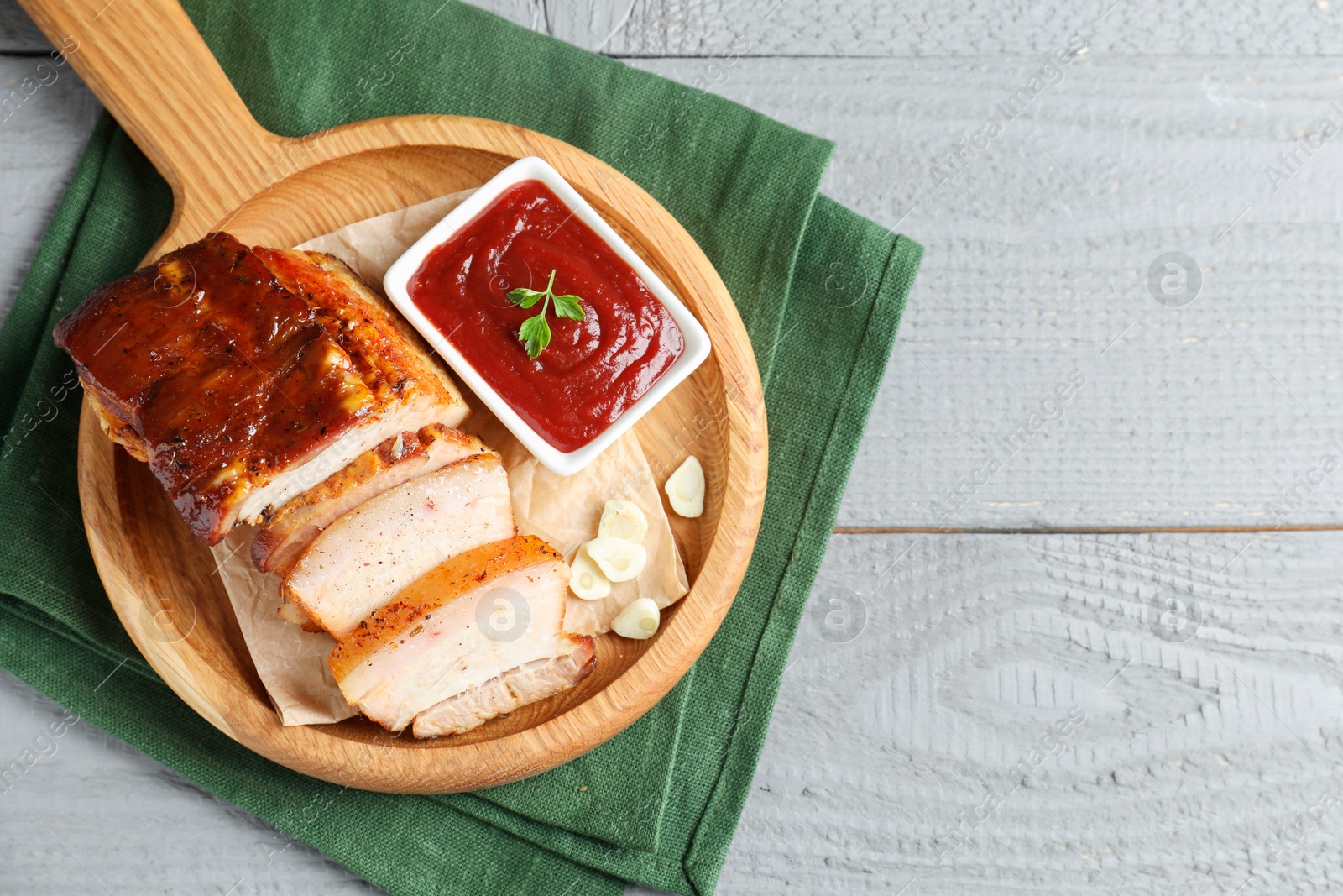 Photo of Pieces of baked pork belly served with sauce on grey wooden table, top view. Space for text