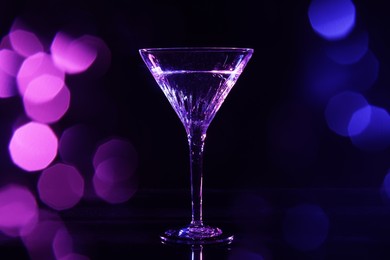 Photo of Glass of martini in neon lights on dark background, bokeh effect