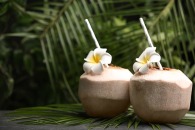 Photo of Young peeled coconut with straws, palm leaf and flowers on black table. Space for text