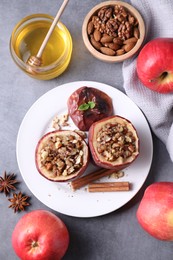 Tasty baked apples with nuts, honey and spices on gray table, flat lay