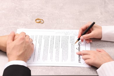 Photo of Man and woman signing marriage contract at light grey table, closeup