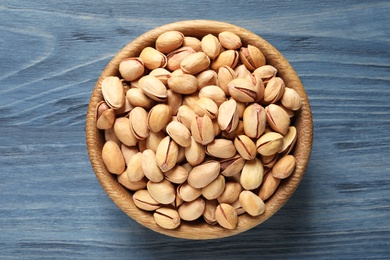 Organic pistachio nuts in bowl on wooden table, top view