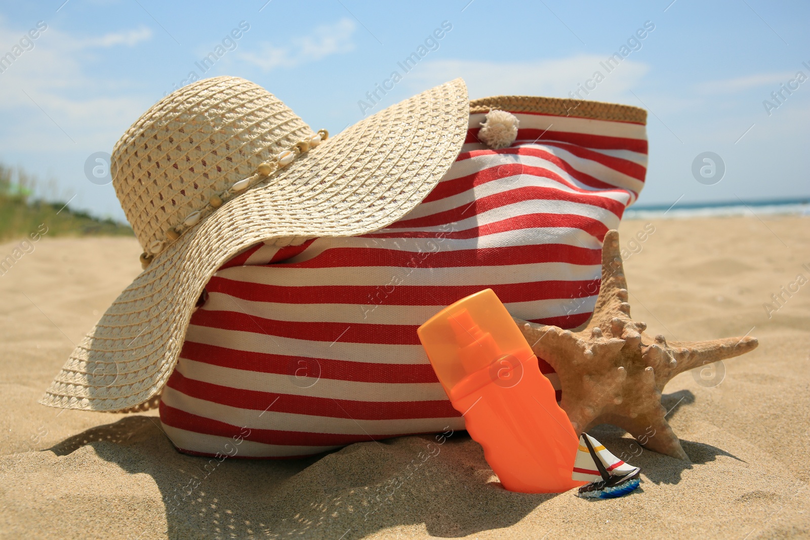 Photo of Bottle of sunscreen, starfish, bag and hat on sand. Sun protection care