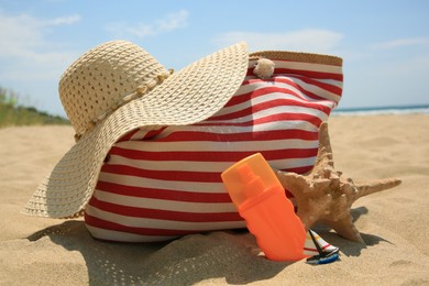 Photo of Bottle of sunscreen, starfish, bag and hat on sand. Sun protection care