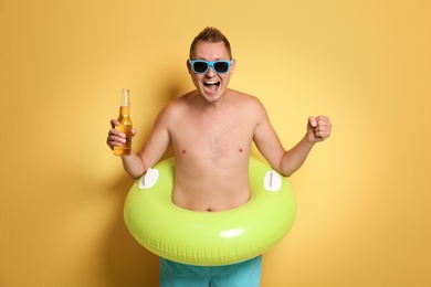 Photo of Shirtless man with inflatable ring and bottle of drink on color background