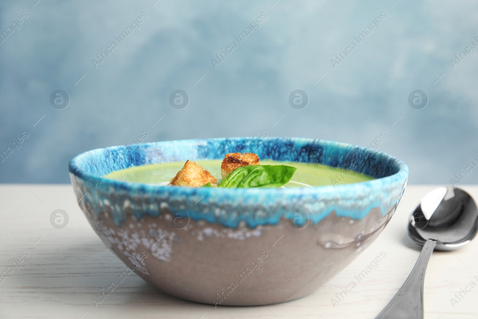 Photo of Delicious broccoli cream soup with croutons served on wooden table against blue background