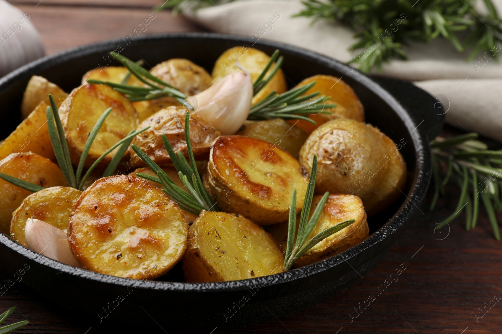 Photo of Delicious baked potatoes with rosemary in frying pan on table, closeup