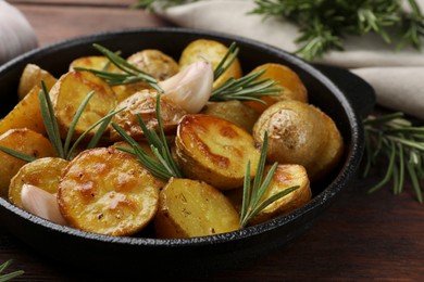 Delicious baked potatoes with rosemary in frying pan on table, closeup