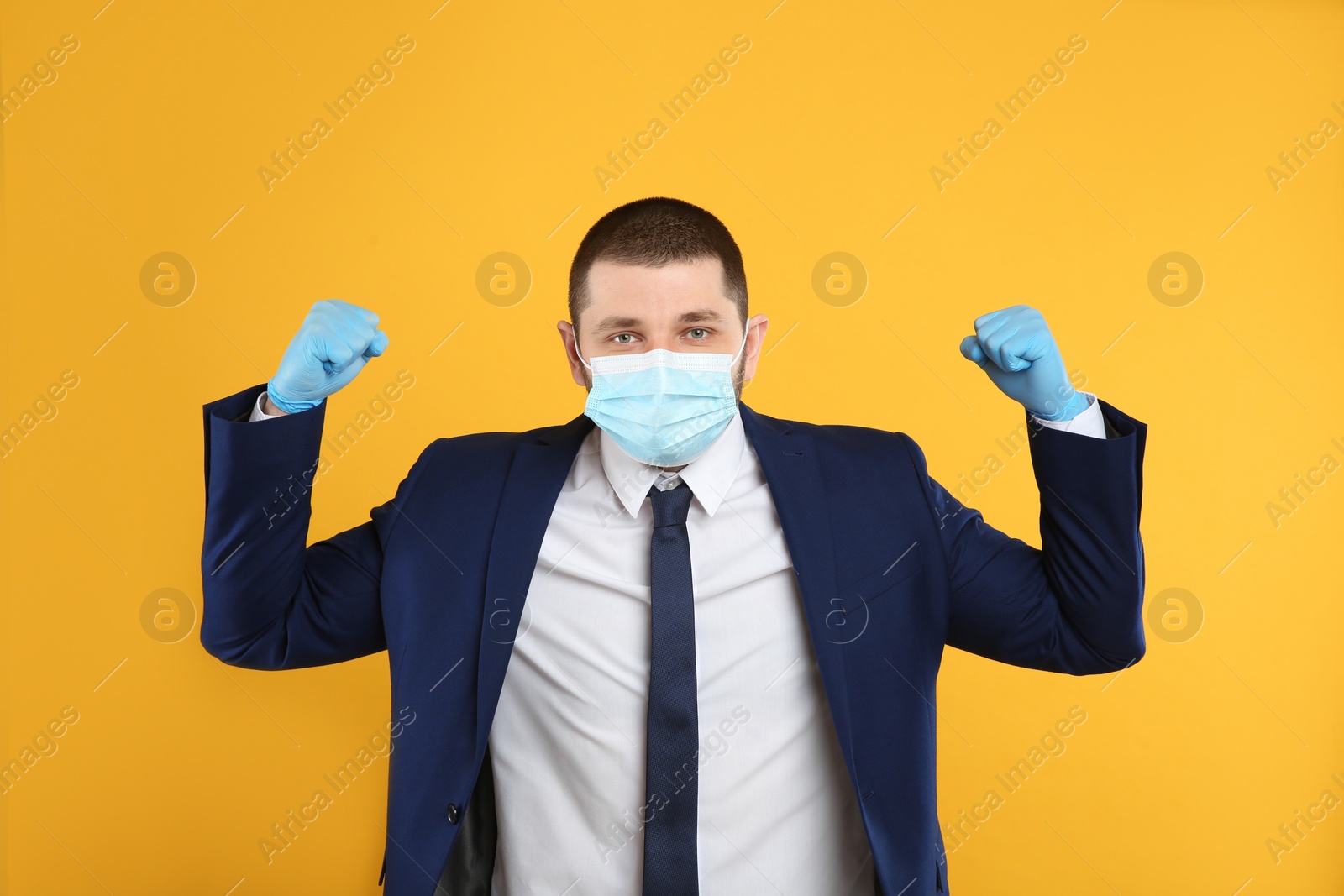 Photo of Businessman with protective mask and gloves showing muscles on yellow background. Strong immunity concept