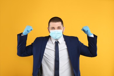 Photo of Businessman with protective mask and gloves showing muscles on yellow background. Strong immunity concept