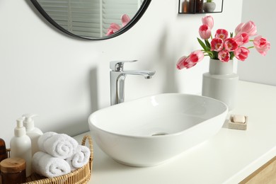 Vase with beautiful pink tulips and toiletries near sink in bathroom