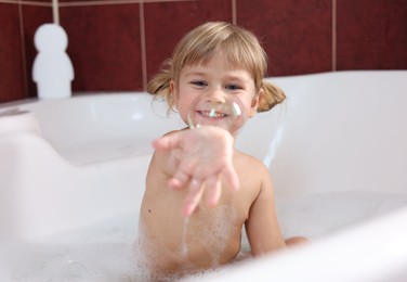 Photo of Smiling girl showing bubble in bathtub at home, selective focus