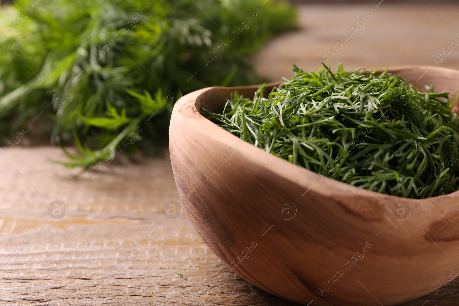 Photo of Fresh cut dill in bowl on wooden table, closeup. Space for text