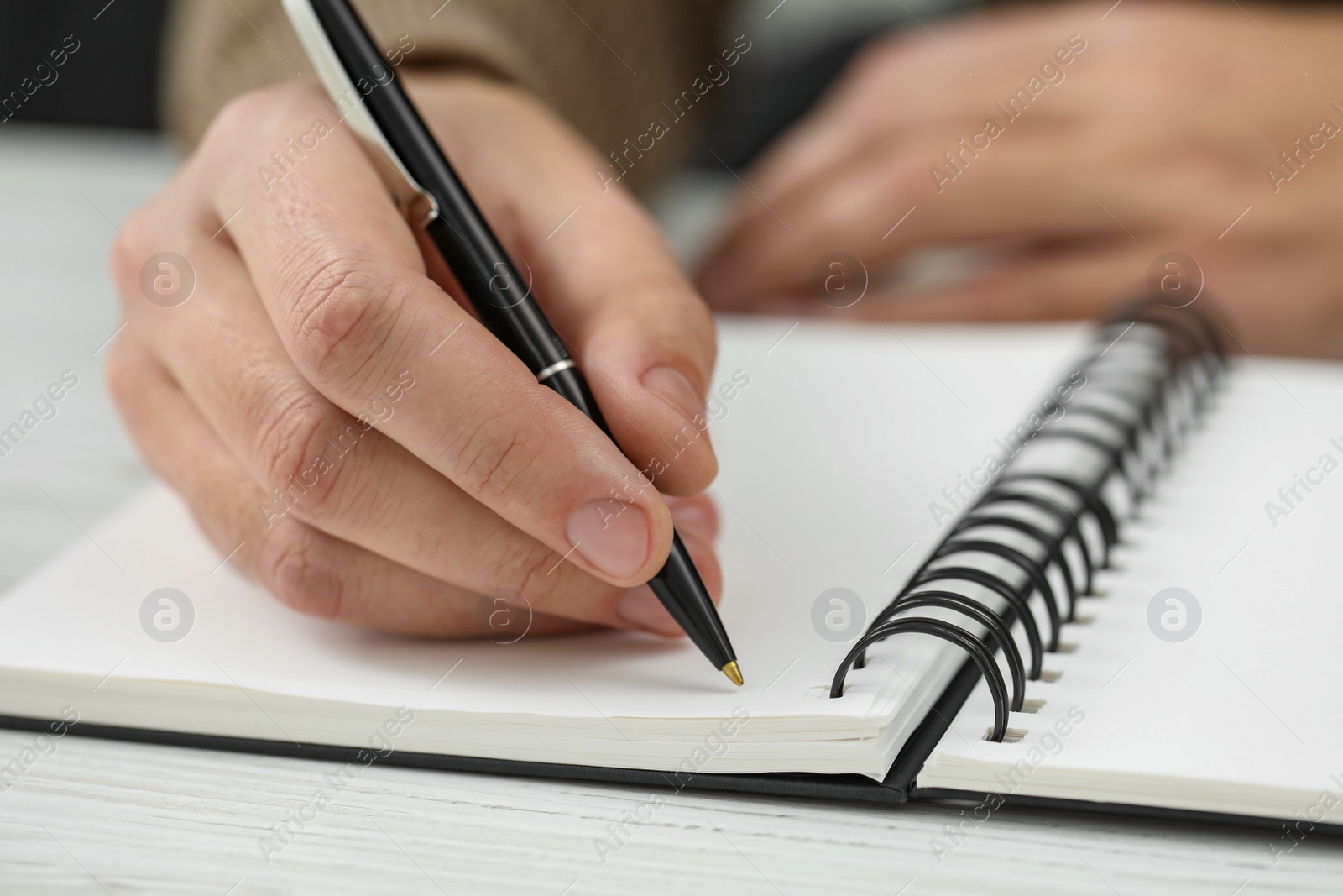 Photo of Man writing in notebook at white wooden table, closeup