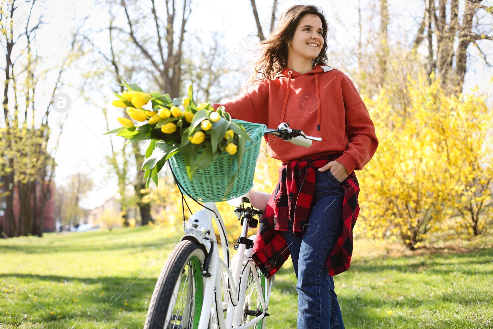 Photo of Beautiful woman with bicycle and bouquet of yellow tulips in park