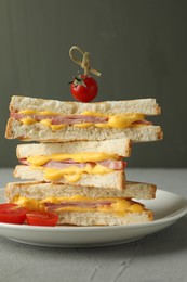 Photo of Stack of tasty sandwiches with ham and melted cheese served with tomatoes on grey textured table, closeup