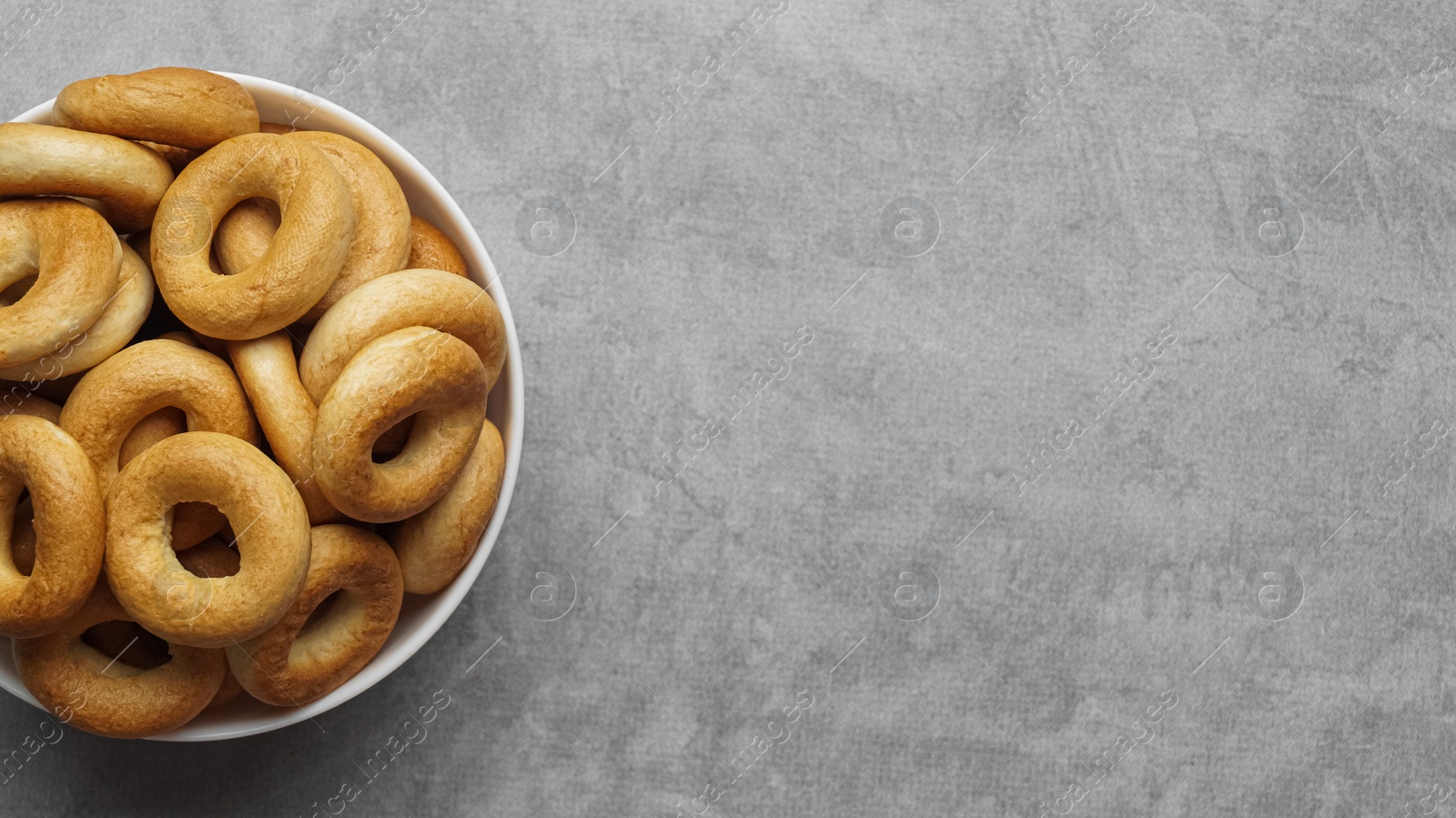 Photo of Bowl of tasty dry bagels (sushki) on grey table, top view. Space for text