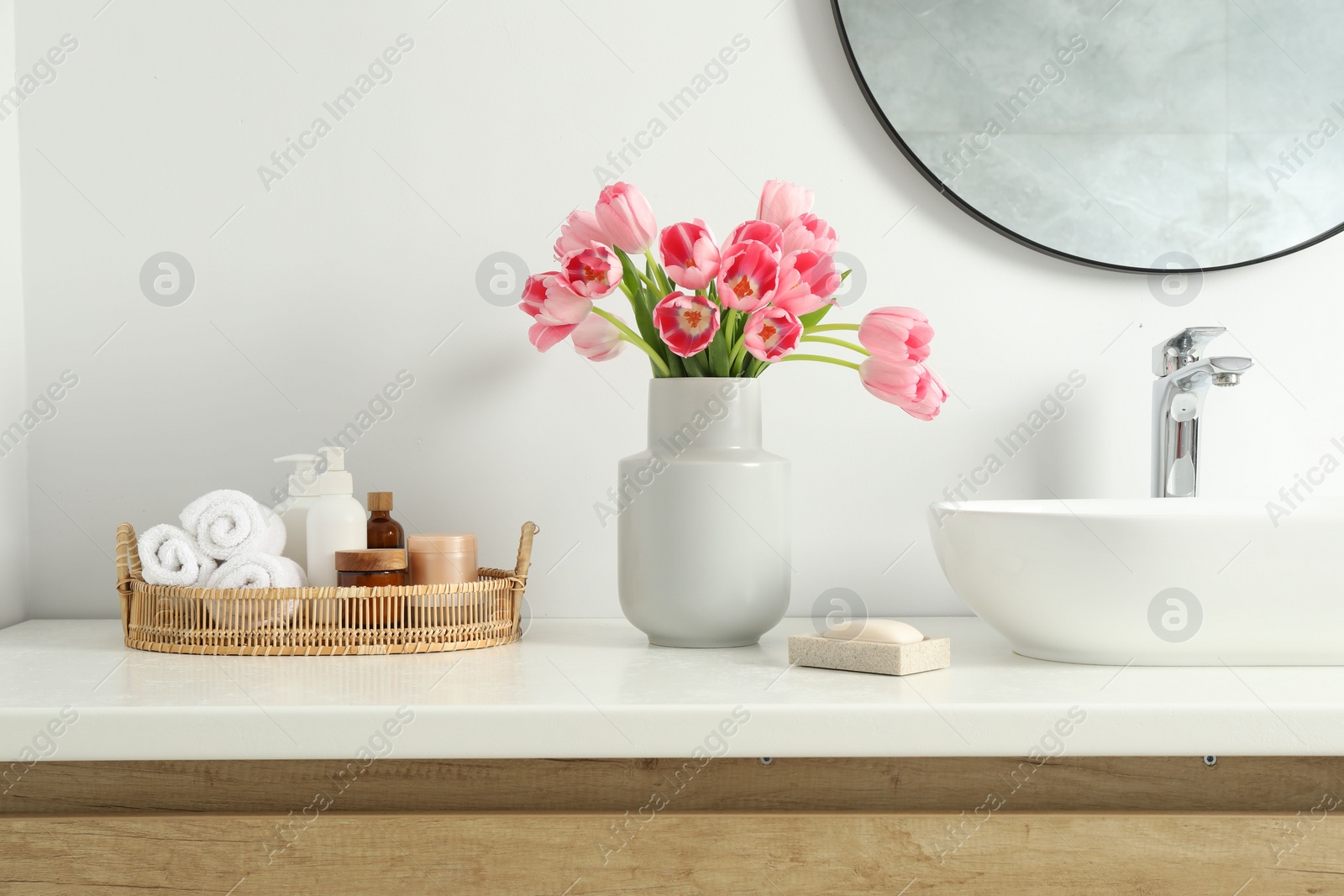 Photo of Vase with beautiful pink tulips and toiletries near sink in bathroom