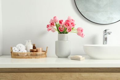 Vase with beautiful pink tulips and toiletries near sink in bathroom