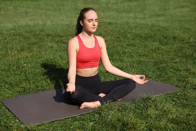 Beautiful woman practicing yoga on mat outdoors. Lotus pose