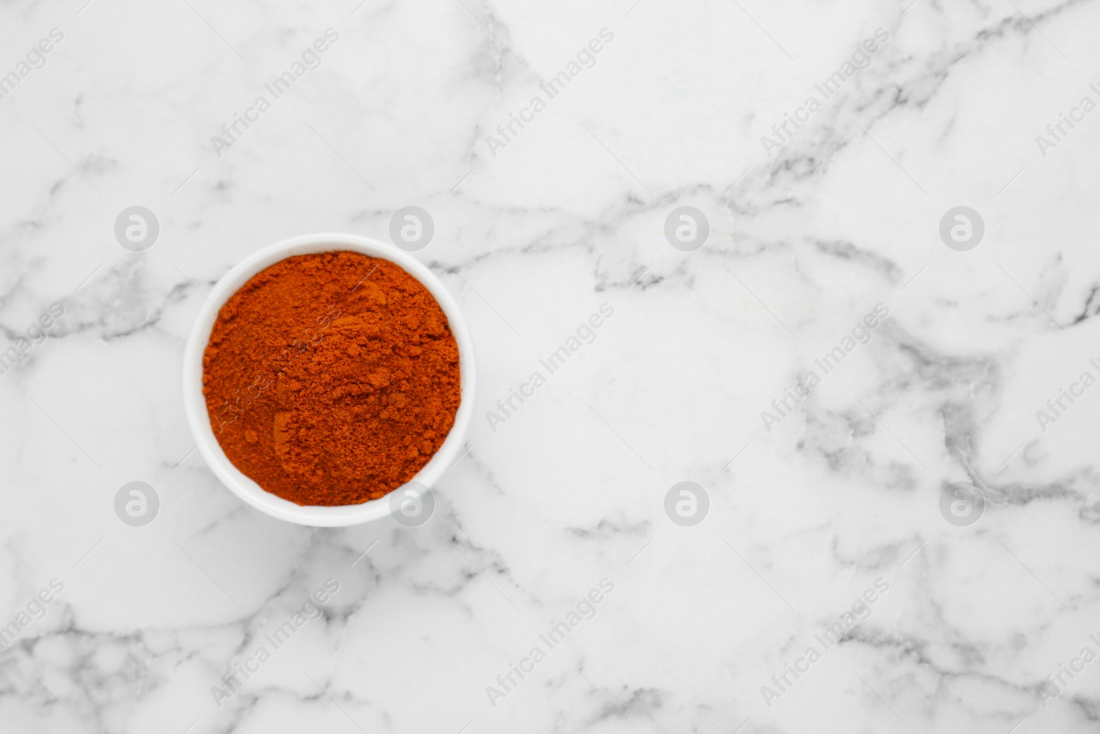 Photo of Bowl with aromatic paprika powder on white marble table, top view. Space for text
