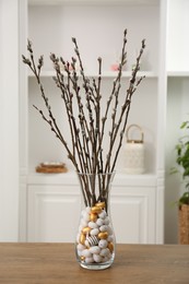 Photo of Beautiful pussy willow branches in vase with painted eggs on wooden table indoors. Easter decor