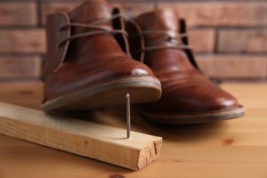 Metal nail in wooden plank and shoes on table