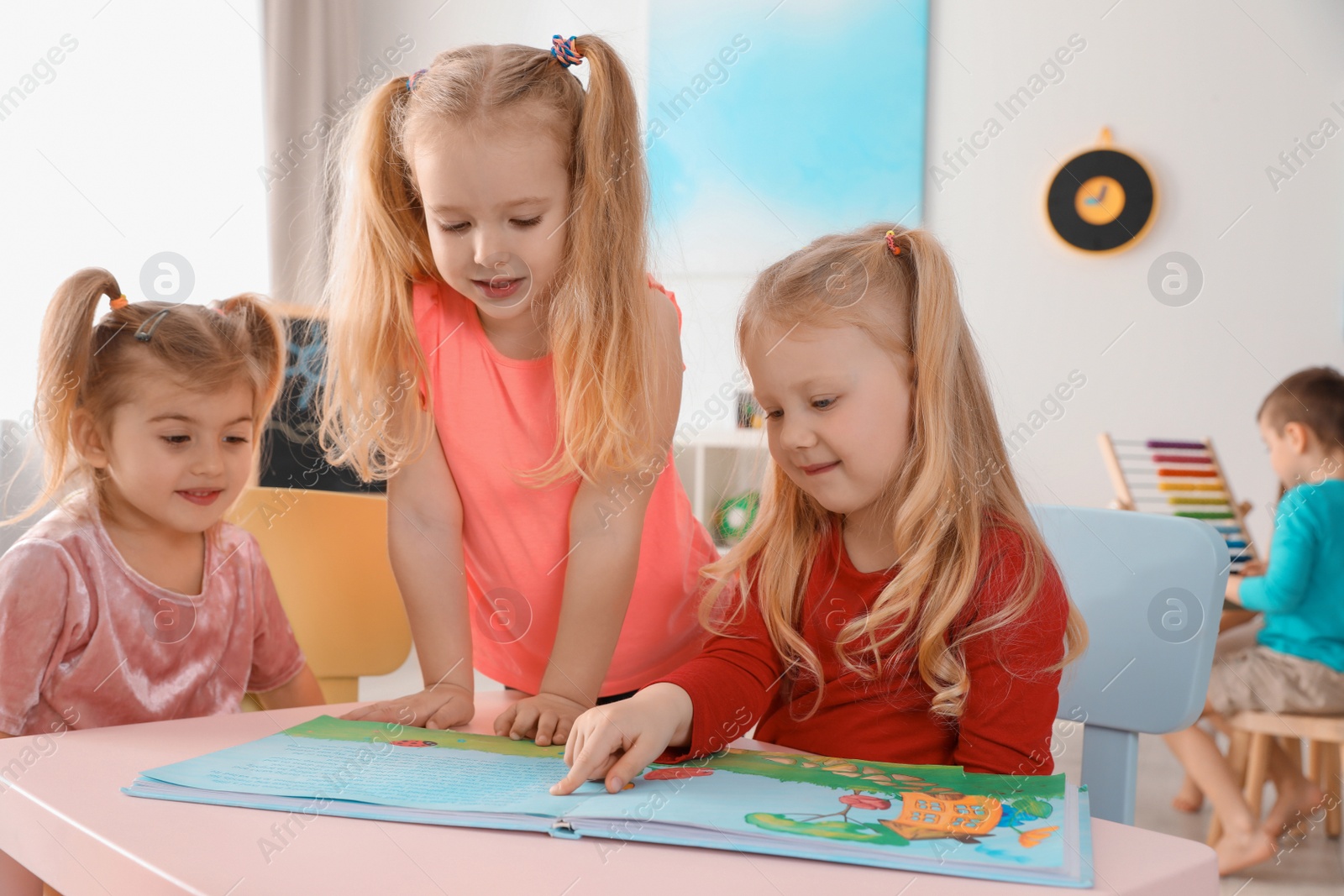 Photo of Cute little children reading book together at table indoors. Learning and playing