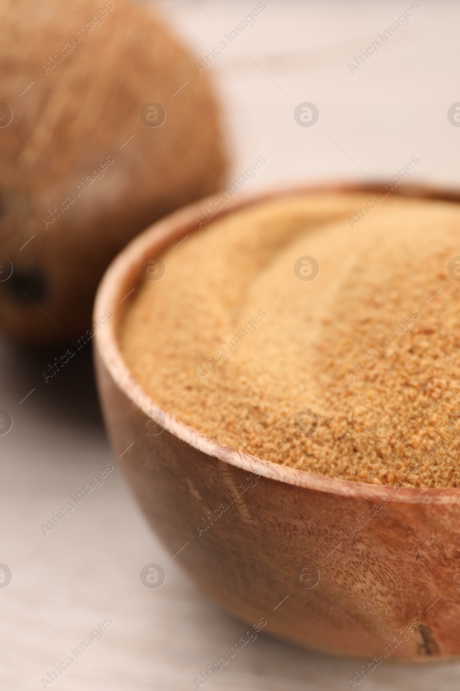 Photo of Coconut sugar in bowl on light wooden table, closeup