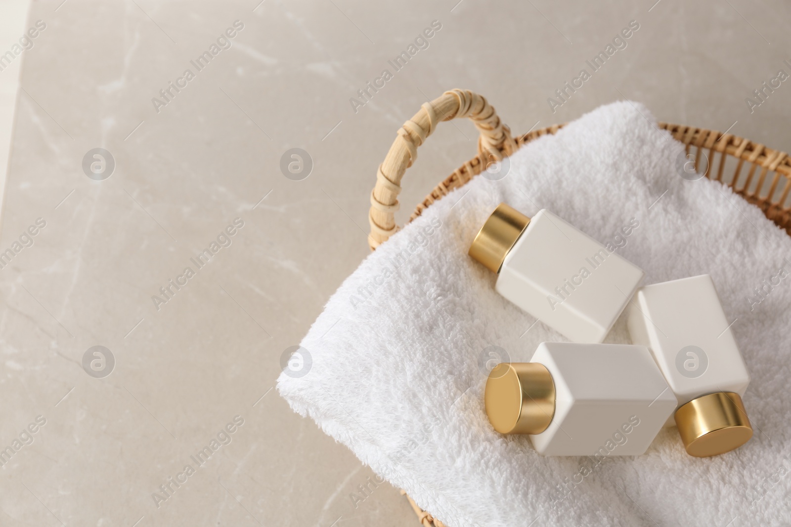 Photo of Wicker basket with fresh towel and cosmetic bottles on light grey table, space for  text. Spa treatment