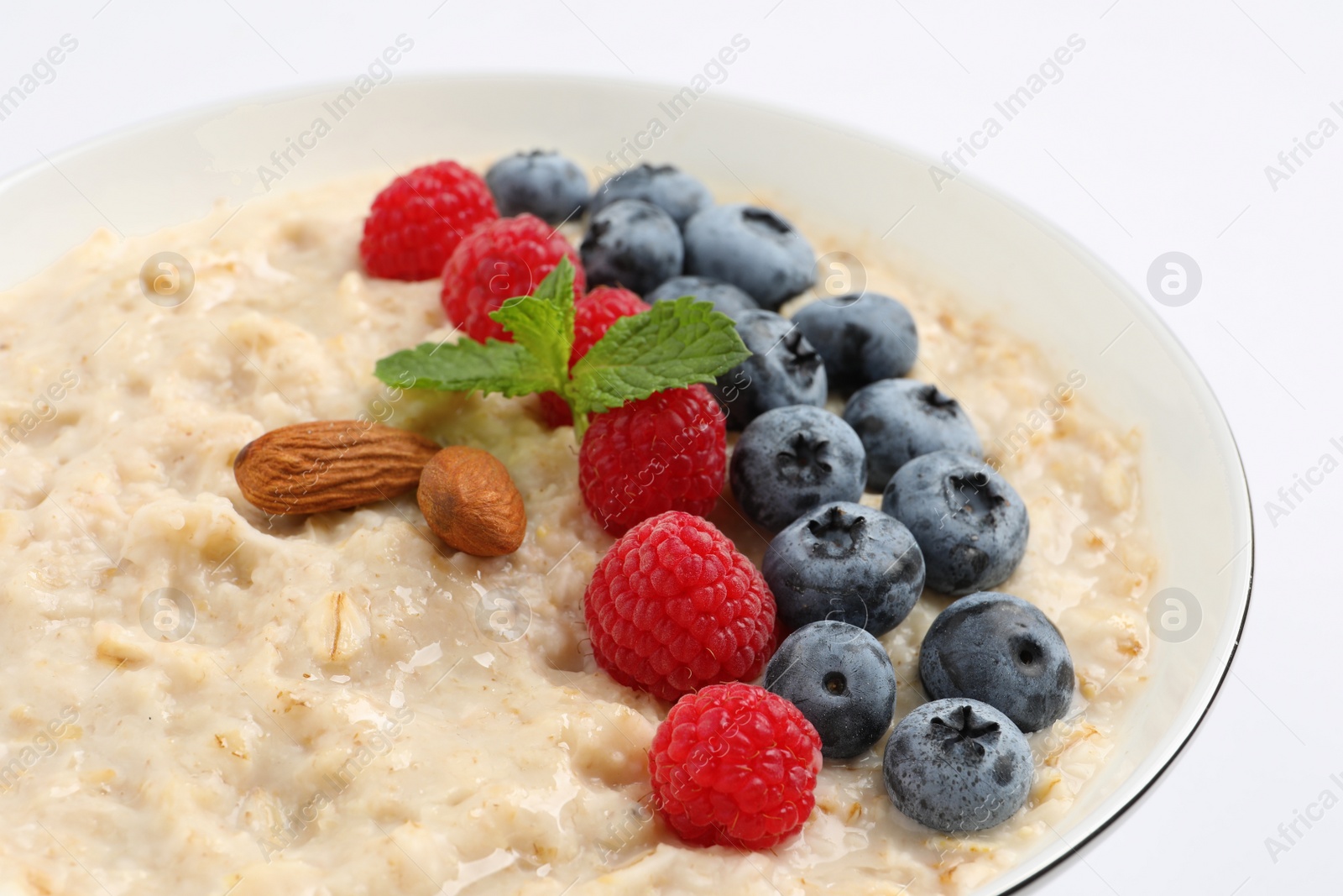 Photo of Tasty oatmeal porridge with raspberries, blueberries and almond nuts in bowl on white background, closeup