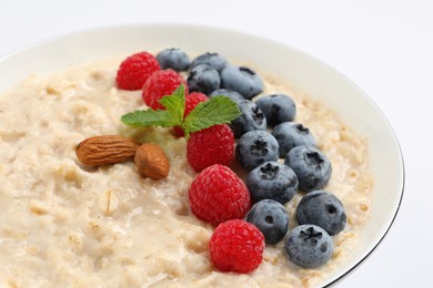 Photo of Tasty oatmeal porridge with raspberries, blueberries and almond nuts in bowl on white background, closeup