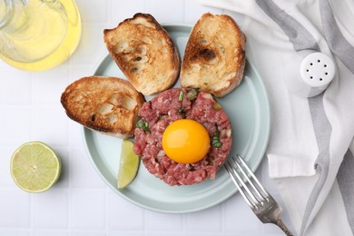 Photo of Tasty beef steak tartare served with yolk, toasted bread and lime on white tiled table, flat lay