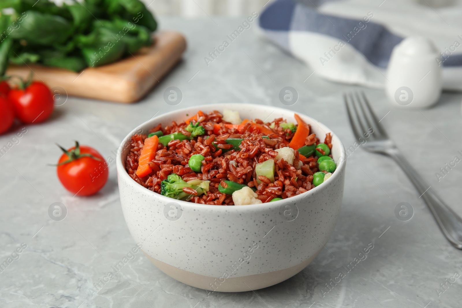 Photo of Bowl of brown rice with vegetables on grey table