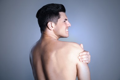 Man suffering from shoulder pain on grey background