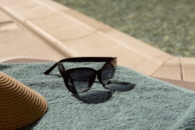 Photo of Stylish sunglasses, visor cap on blue towel near outdoor swimming pool, closeup